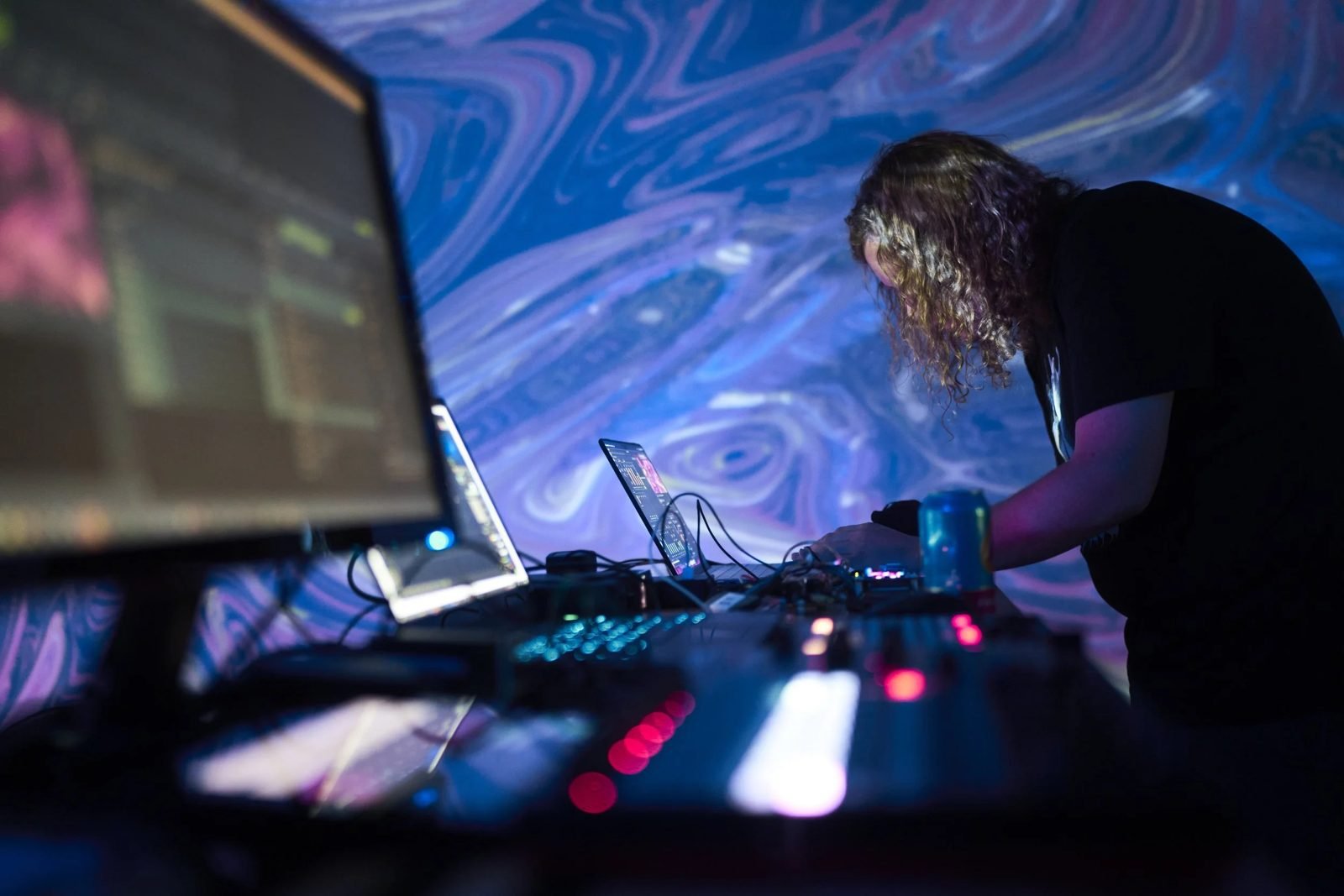 A DJ at a controller with marbled blue projection filling the wall behind